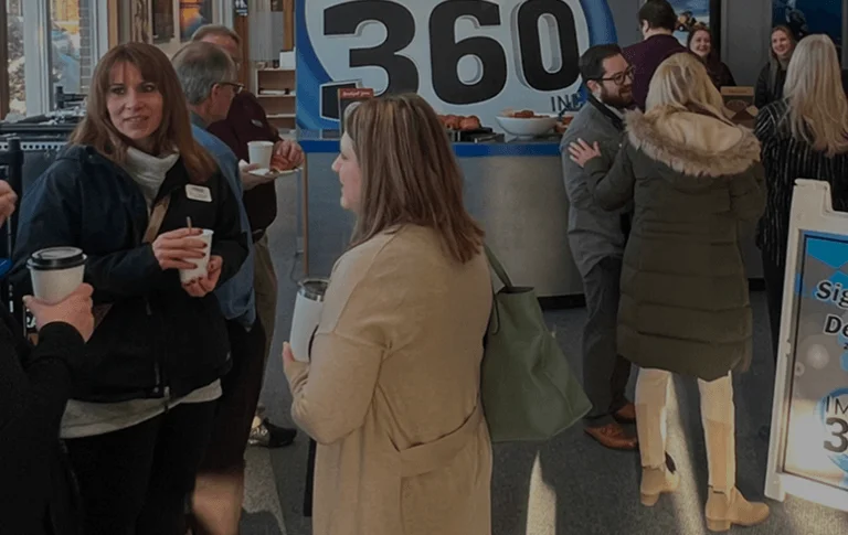 A group of people mingles at an event, enjoying refreshments and chatting near a display featuring "Image 360" signage.