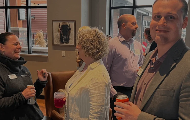 A group of people socialize in a modern venue, enjoying drinks and engaged in conversation amidst large windows and stylish decor.