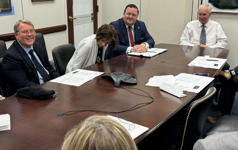 A group of professionals engaged in discussion around a conference table in a well-lit meeting room