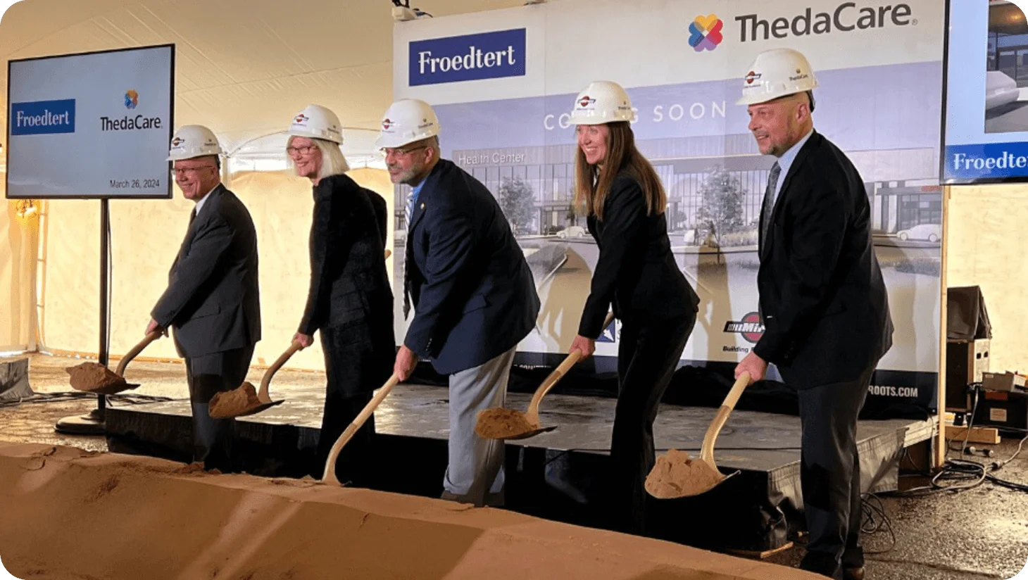 Five individuals in hard hats hold shovels at a groundbreaking ceremony for a new Froedtert and ThedaCare Health Center, scheduled for 2024.