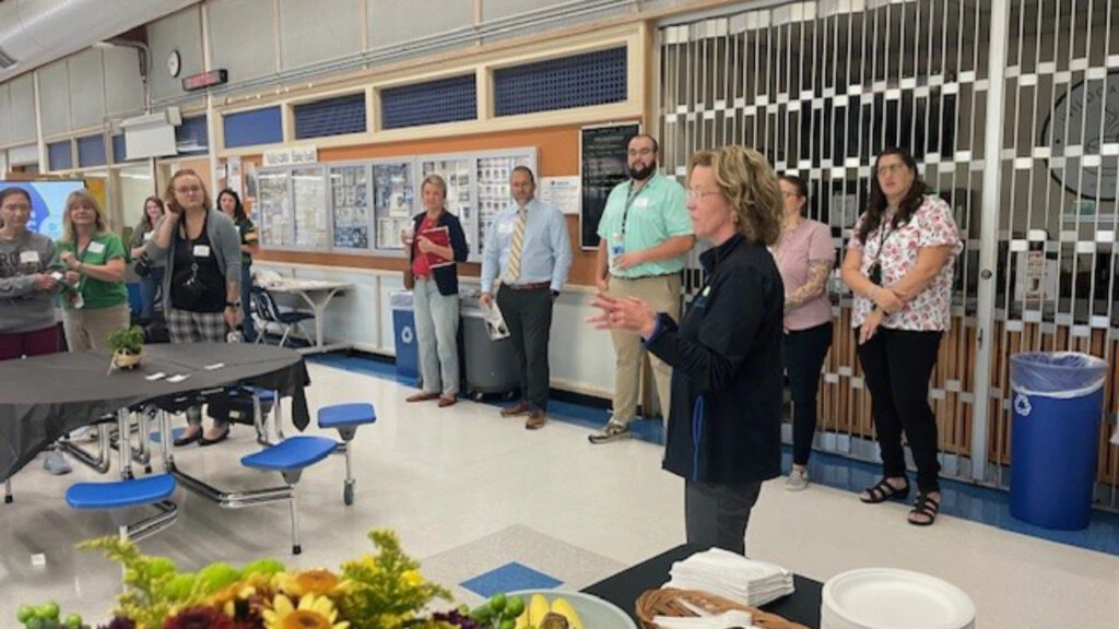A woman addresses a group of people, standing in front of them with a focused expression and open body language
